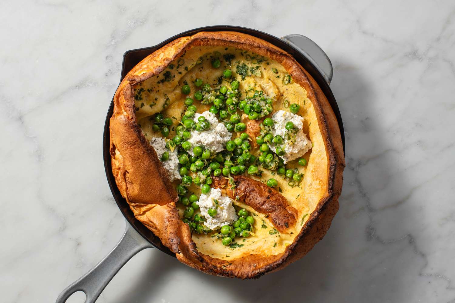 Un Dutch Baby garni de fromage Boursin et de petits pois cuits
