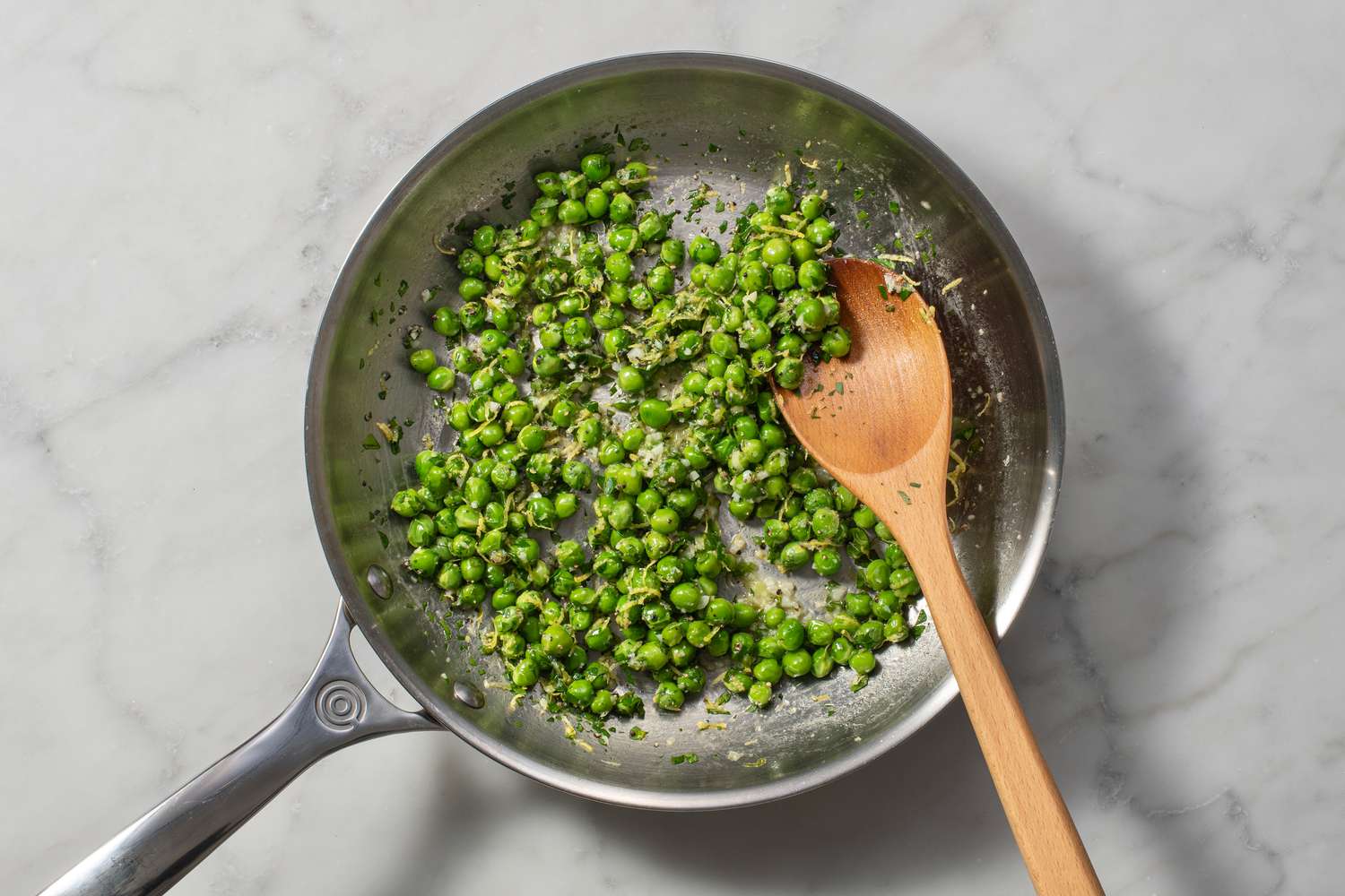 Persil, sel, poivre et zeste de citron ajoutés dans la poêle de petits pois cuits